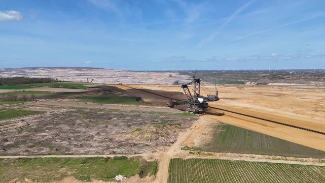 bucket wheel excavator sits where hambach coal mine meets farmland cleared stump ground gives way to rows of green crops conveyor belt cuts across boundary wind turbines dot ridge kerpen germany