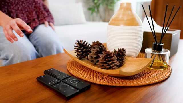 Woman sitting on sofa and picking up remote control from coffee table with modern home decor.