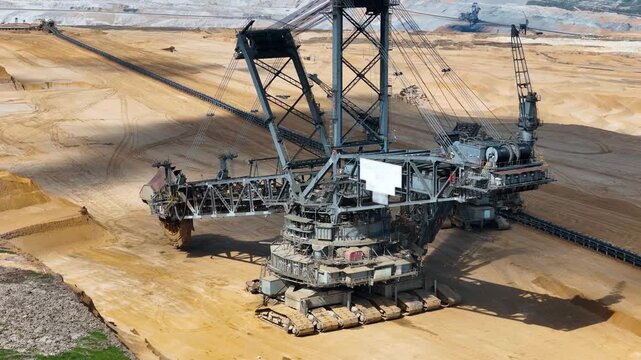 bucket wheel excavator boom swings above hambach lignite mine steel lattice framework conveyor system crawler tracks visible in close aerial orbit near kerpen germany surface coal mining scale