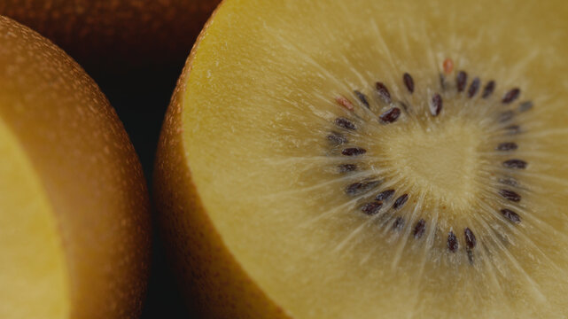 Extreme macro shot of halved ripe golden kiwis filling the frame, showing juicy pulp and seeds texture under artistic lighting. Perfect for healthy eating, gourmet food, and culinary concepts.