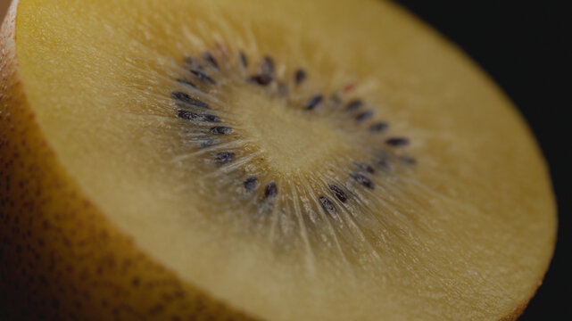 Extreme macro shot of a halved ripe golden kiwi with selective focus on the pulp and seeds, showing a rich juicy texture under artistic lighting for healthy eating, gourmet food, and culinary concepts