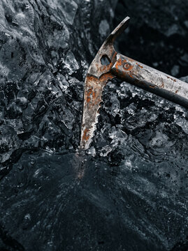 rusty vintage ice axe embedded into thick clear glacier ice during extreme winter mountaineering adventure close up detailed view in harsh cold mountain peak rock climbing gear safety