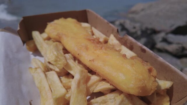 Box of Fish and Chips at the beach in Newquay, Cornwall, England on a hot sunny day.