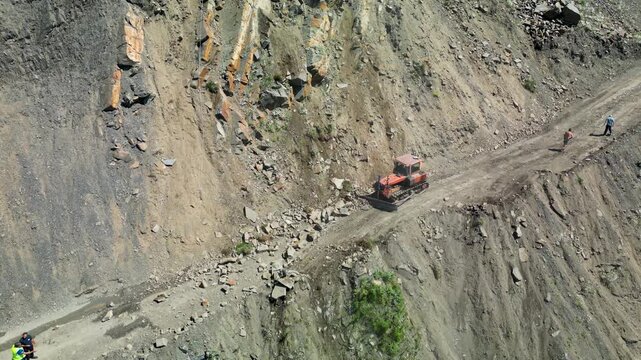 Drone footage of an excavator clearing rocks from a mountain road after rockfall in the Caucasus Mountains of Georgia.