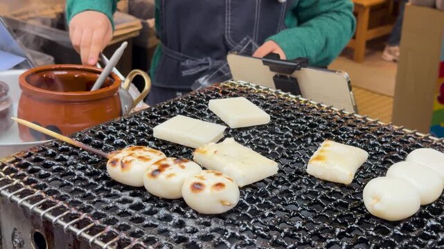 Chef grilling traditional japanese mochi and dango rice cakes on charcoal grill at street market.