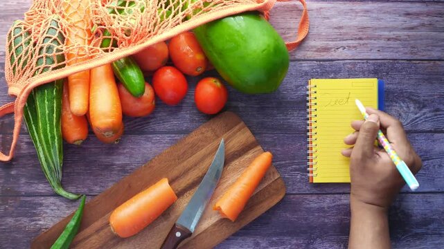 Overhead view of person writing diet plan next to fresh vegetables in a bag