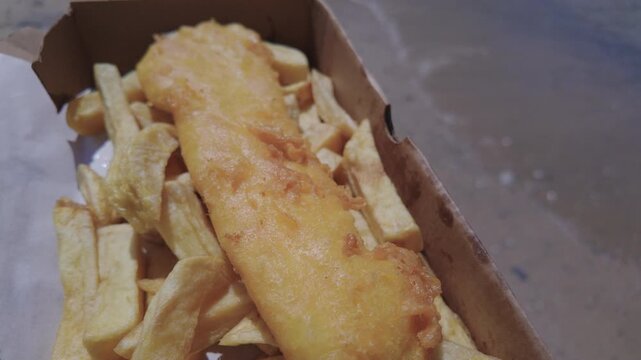 Box of Fish and Chips at the beach in Newquay, Cornwall, England on a hot sunny day.