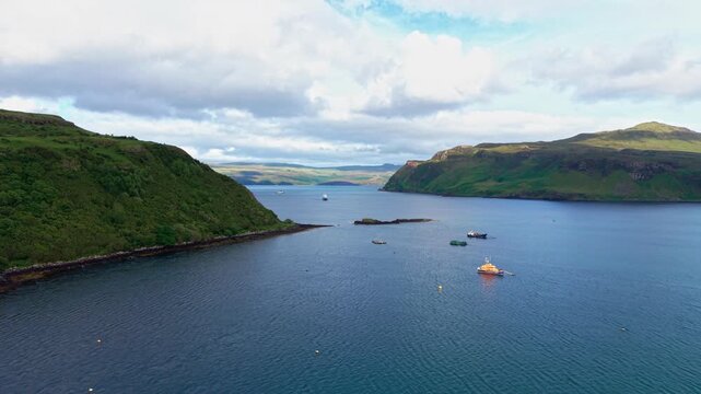 Aerial drone view over Loch Portree on the Isle of Skye in Scotland, United Kingdom, with boats on calm turquoise water between green hills under cloudy skies. 4K UHD video.