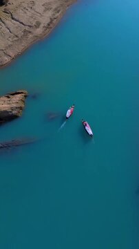 Aerial view of two traditional wooden boats sailing on a vibrant turquoise river