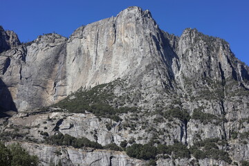 Fototapeta premium Sunlit Granite Mountain Peak and Sheer Rock Face Under Clear Blue Sky in Yosemite Valley