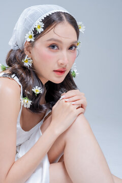Gentle innocent woman with daisy flowers in hair crouching delicately, embracing pure tenderness, botanical skincare beauty, youthful fragility, poetic romance, peace, and angelic spring serenity.