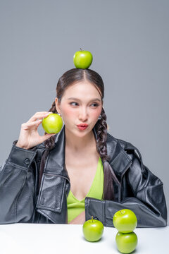 Trendy stylish woman balancing green apple on head, showcasing playful attitude, fashion beauty, quirky balance, youthful confidence, creative diet concept, modern wellness, and edgy cool lifestyle.