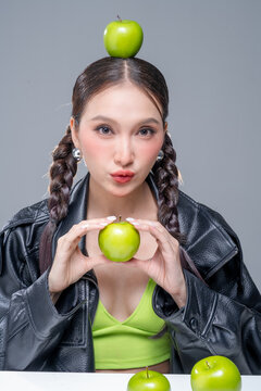 Trendy stylish woman balancing green apple on head, showcasing playful attitude, fashion beauty, quirky balance, youthful confidence, creative diet concept, modern wellness, and edgy cool lifestyle.