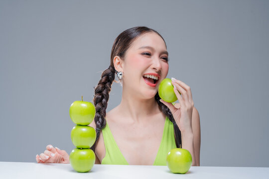 Radiant cheerful woman holding fresh green apple, expressing healthy lifestyle, organic diet vitality, dental beauty, wellness balance, joyful nutrition, natural freshness, and vibrant body detox.