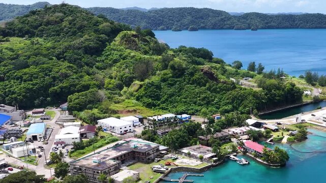 Aerial view of Malakal harbor and coastal industrial buildings in Koror Palau with lush green mountains and blue ocean.