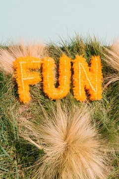 Beaded yellow letters spelling fun resting in soft tufted grass with bright cheerful lighting for creative social media and lifestyle content