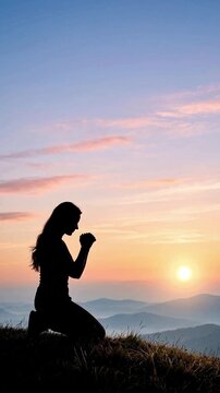 Silhouette of a woman kneeling and praying on mountain top at sunrise