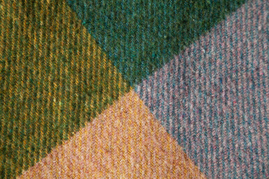 Close-up of authentic vintage wool cashmere with geometric color-block pattern in green, blue, yellow and muted pink. Soft textured woven fabric with natural fibers and rich color transitions. 