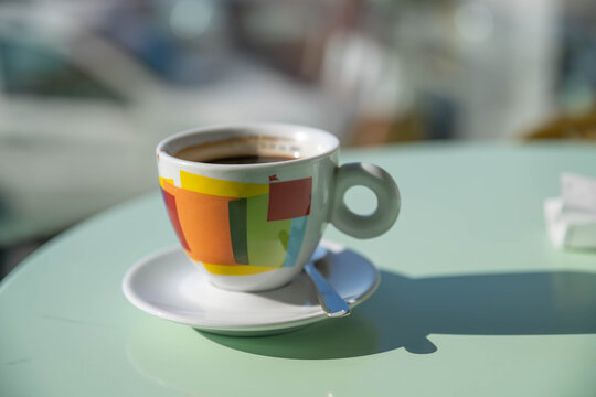Americano served in a geometric patterned cup, casting a strong shadow across a pastel green cafe table