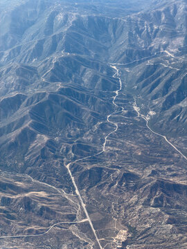 Aerial view of a rugged canyon with a pale riverbed snaking between forested ridge lines and a straight road below, Acton, California