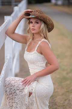Blonde woman wearing cowboy hat posing by fence