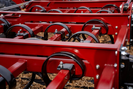 Close-up of black spring tines and metal rings mounted on red steel frame of agricultural cultivator machine.