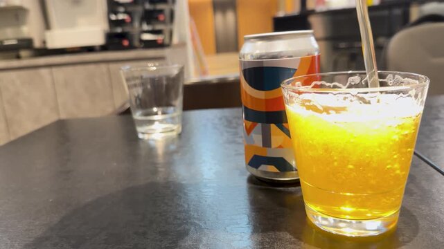 Pouring golden beer into glass next to can on dark table slow motion.