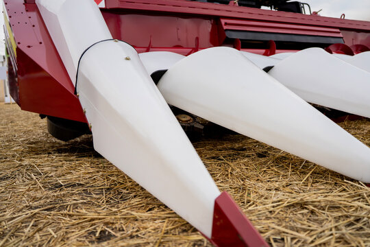 Front view of white snouts on corn header attachment of agricultural combine harvester over straw ground.