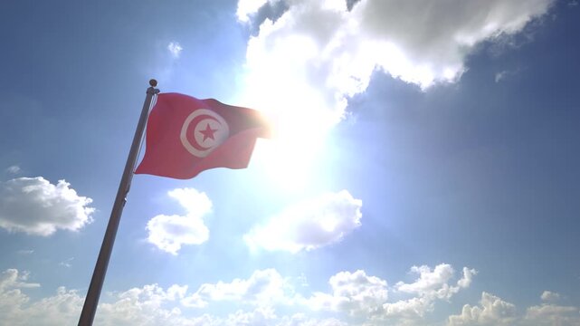 Tunisia Flag waving on a Flagpole from a Moving Angle in front of a blue sky with clouds	