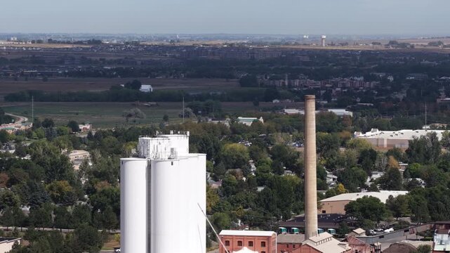 Aerial of industrial complex and residential area in Loveland Colorado with white storage tanks and prominent brick smokestack