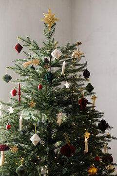 Beautiful Christmas tree decorated with paper toys, candles and gold star topper. Vintage Christmas tree decor, Scandinavian holiday style, warm festive mood.