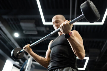 Athletic man performing barbell curl exercise in modern gym interior. Strength training and...