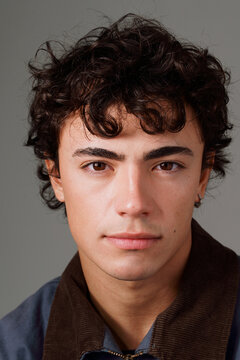 Young Man With Curly Hair Poses Against a Simple Backdrop