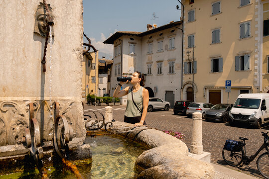 Woman cyclist drinking water in italian village square