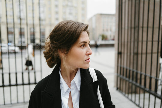 Woman Gazing Thoughtfully Through an Iron Gate in a City