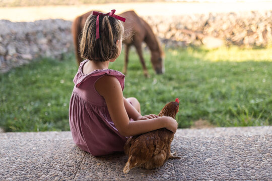 Little girl stroking brown hen next to egg basket at patio