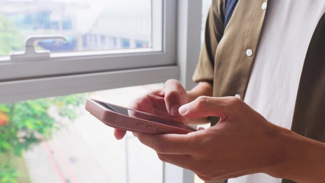 Reviewing work messages on a smartphone while waiting for a train by a window in a modern station