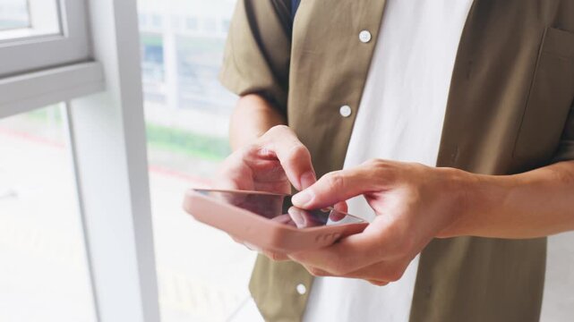 Reviewing work messages on a smartphone while waiting for a train by a window in a modern station