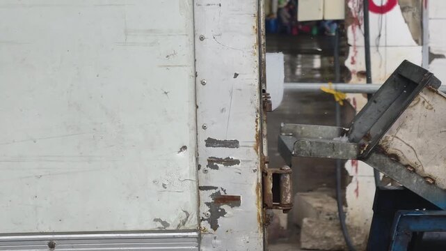 A metal hook lowering a large ice block inside a refrigerated truck next to an active ice crusher machine at a port