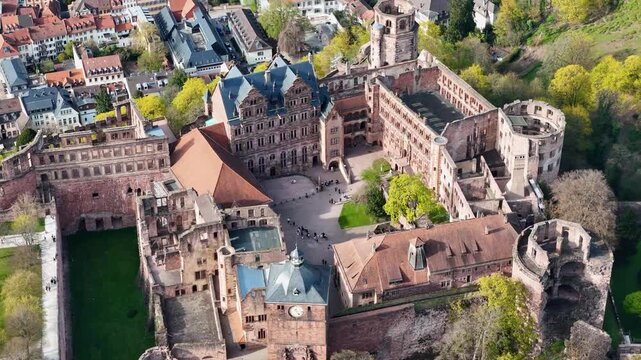 heidelberg castle ruins crown wooded hillside above old town rooftops renaissance courtyard clock tower round tower fortress walls tourists plaza wide aerial pullback drone footage germany baden