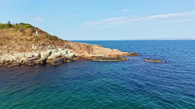 Waves gently lap against the rocky shoreline. A grassy hill rises above the water, creating a natural border. The sky is clear with few clouds visible.