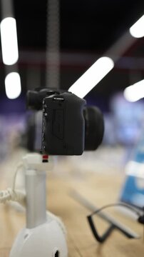 Vertical screen digital camera with zoom lens displayed on security stand in electronics store featuring modern photography equipment for content creation and travel work
