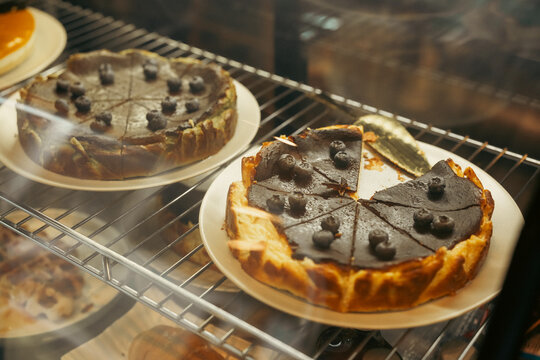 Chocolate cheesecake with blueberry topping cooling on ceramic plates inside glass oven, showing baked dessert preparation and warm kitchen atmosphere