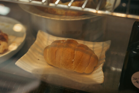 Fresh bread loaf in bakery display case with warm golden crust, wooden serving plate, and stainless steel oven background creating inviting view of baked food