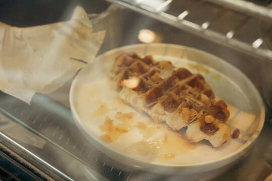Golden waffle with caramel sauce on ceramic plate inside countertop oven, warm dessert scene with crisp texture and appetizing presentation