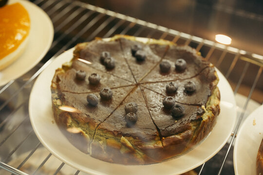 Chocolate cheesecake with blueberry topping displayed on white plate inside bakery display case