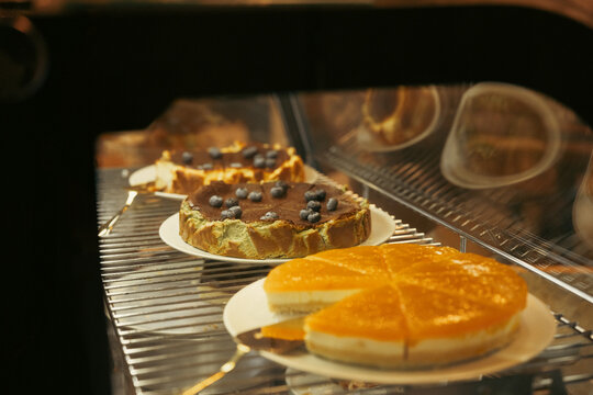 Orange cake and blueberry pastry cooling on wire rack inside oven with warm golden light and visible baking texture, creating cozy homemade dessert scene