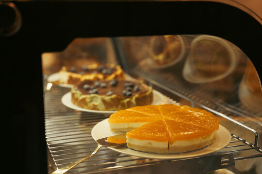Fresh citrus cheesecake and baked pastry on plate inside warm oven, showing golden crust, creamy filling, orange topping, and appetizing homemade dessert detail