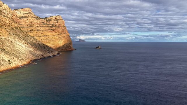 Sunlit Headland Against Clouded Sky With Calm Sea, Sheer Sandstone Cliff, Distant Islet And Peaceful Shoreline