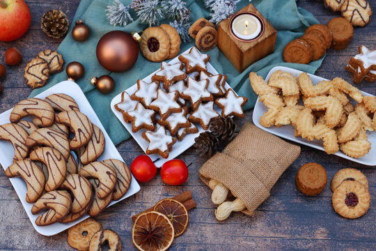 A festive flat lay featuring various Christmas cookies, such as cinnamon stars, shortbread cookies, peanuts, and a lit candle.
